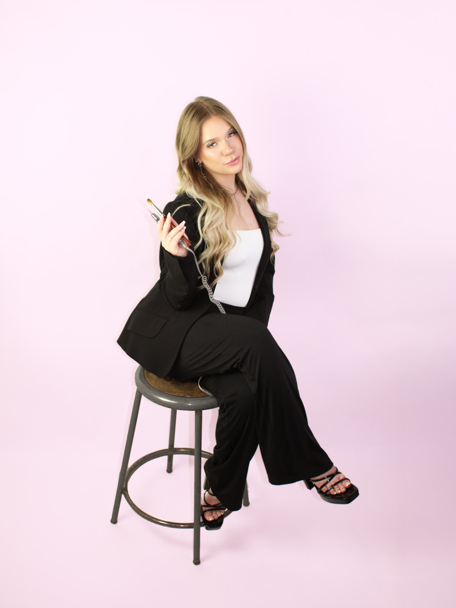 A photo of Lexie sitting on a stool holding some of her nail tools