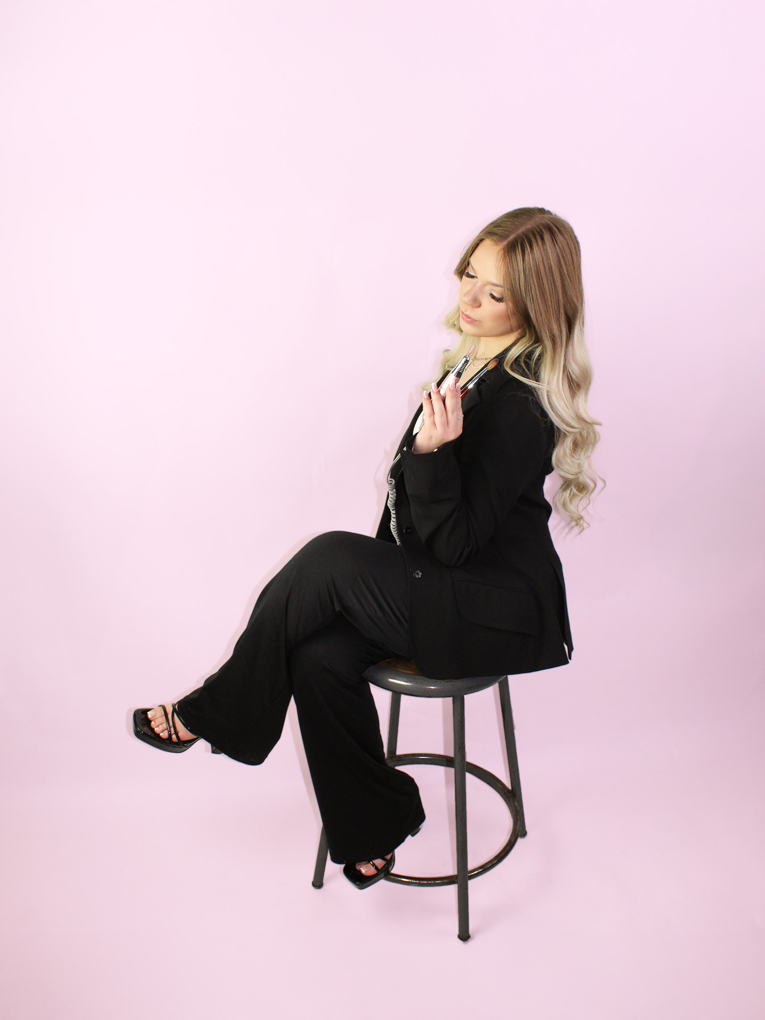 A photo of Lexie sitting on a stool looking down holding some of her nail tools